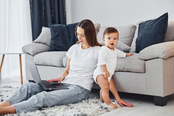 Silver colored laptop. Mother with her little daughter is indoors at home together