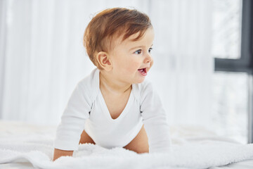 Fototapeta premium Playing on the bed. Cute little baby is indoors in the domestic room