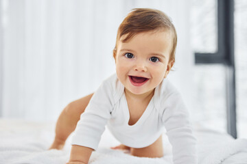 Fototapeta premium Playing on the bed. Cute little baby is indoors in the domestic room