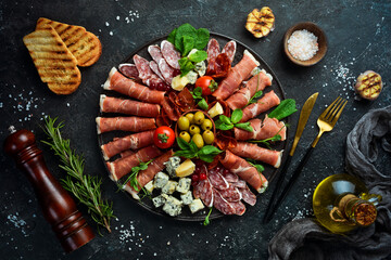 Italian prosciutto, dried pork, parmesan cheese, olives and snacks on a plate. Top view. On a gray...