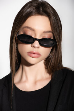 portrait of young brunette woman posing in black sunglasses isolated on grey.
