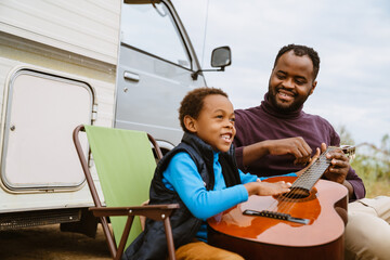 Black man teaching his son to play guitar during journey on trailer