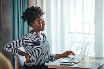 Tired african American millennial female worker sit at desk touch back suffer from lower spinal spasm, hurt unhealthy biracial woman stretch have strong backache, incorrect posture concept - Powered by Adobe