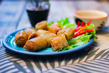 Deep fried spring rolls in blue plates with vegetables, chili and dipping sauce (Chinese food)