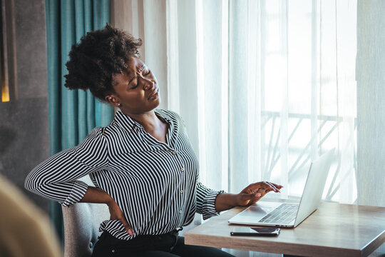 Tired African American Millennial Female Worker Sit At Desk Touch Back Suffer From Lower Spinal Spasm, Hurt Unhealthy Biracial Woman Stretch Have Strong Backache, Incorrect Posture Concept