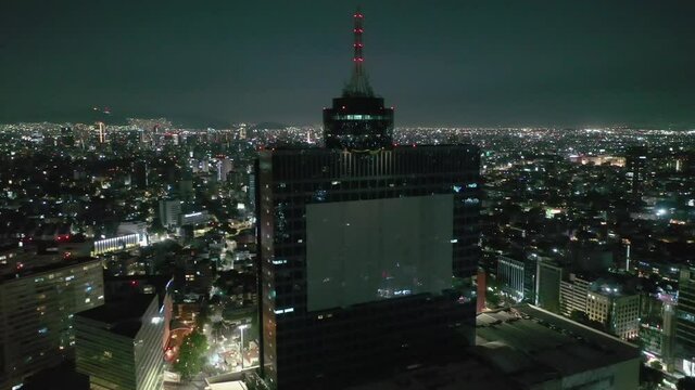 Orbit over Mexico City lit up at night with WTC downtown cityscape skyline and Reforma towers, Aerial