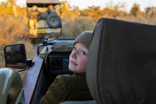 A boy in a hat and coat in a jeep at sunrise on a safari drive. 