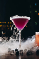 Smoking martini glass with purple drink. Cocktail with blueberries 