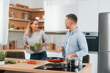 Talking with each other. Couple preparing food at home on the modern kitchen