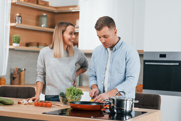 Fototapeta na wymiar Talking with each other. Couple preparing food at home on the modern kitchen