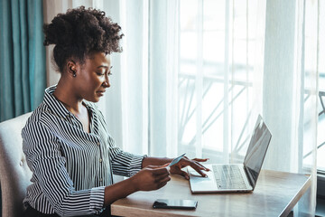 Young woman holding credit card and using laptop computer. Businesswoman working at home. Online shopping, e-commerce, internet banking, spending money, working from home concept