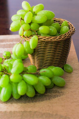 Green Grape placed in a woven basket and a wooden table top.