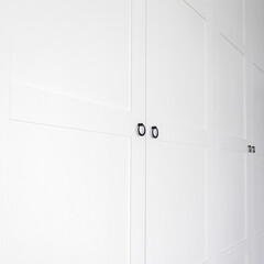 White vintage wardrobe with crown moldings wooden shelves and drawers and open facade door in light empty room