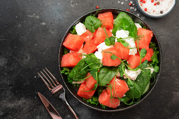 Summer watermelon salad bowl with goat cheese, spinach and pea sprouts on gray table background, top view, copy space