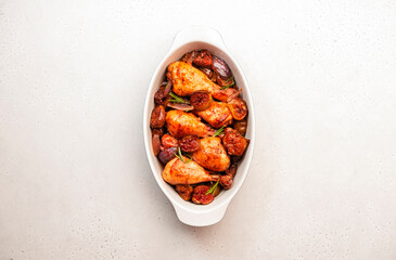 Baked chicken legs, drumsticks with figs and red onions in ceramic baking dish, white kitchen table background, top view