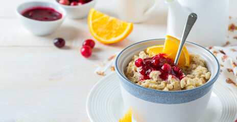 Oat porridge with cranberry sauce and orange in a ceramic bowl for healthy breakfast on a light background. Selective focus.