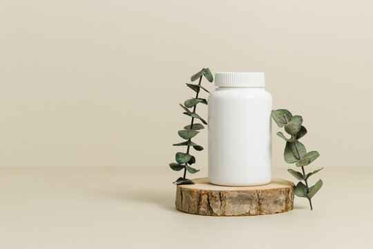 Medicine bottle for vitamins or pills on wooden podium with eucalyptus leaves, natural supplement, organic vitamins, bottle mockup, copy space