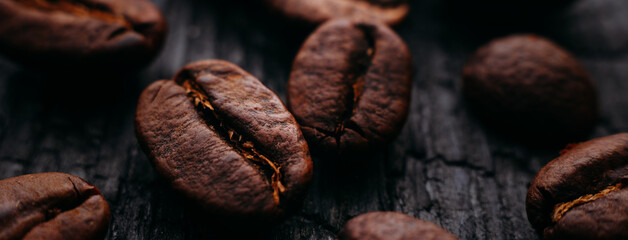 Advertising banner of coffee roasted beans close-up. Coffee on a dark background of burnt wood. Macro photography.