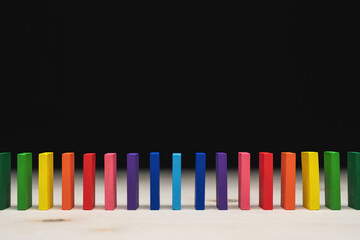 Colored dominoes lined up in a row by rainbow color. Light foreground and black background with copy-space. 