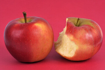 Pomme entière et pomme croquée en gros plan sur fond rouge
