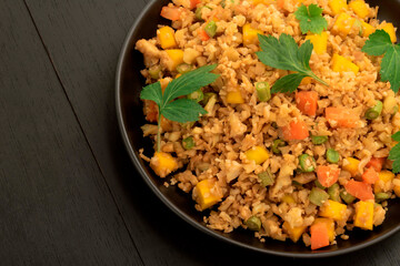 Cauliflower fried rice has vegetable in black dish on wood table.