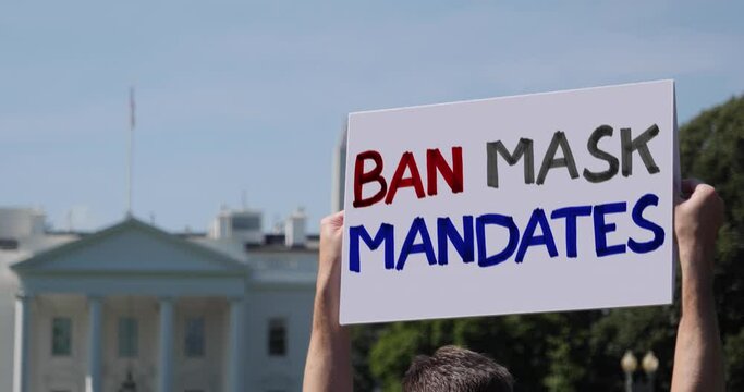 A man holds a BAN MASK MANDATES protest sign outside of the White House.  