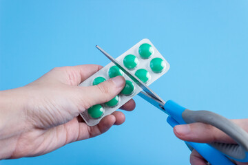 Scissors in hands cut a blister with medical pills on a blue background close-up. The concept of...