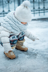child squats and draws something in the snow, a kid is dressed in a white jacket, pants with a...