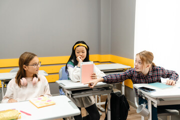 Multiracial girls talking and sitting at desks during class