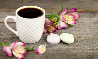 Fototapeta na wymiar Cup of coffee, flowers and meringue on a wooden textured table. Sweet breakfast