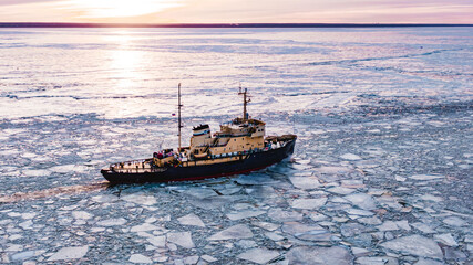 Icebreaker goes on the sea among the blue ice at sunset, aerial view - obrazy, fototapety, plakaty