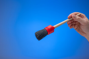 Dusting brush with wooden handle held by male hand. Close up studio shot, isolated on blue background