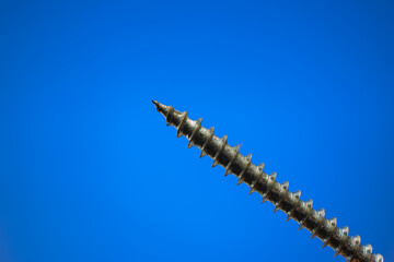 Small metal threaded screw. Close up studio macro shot, isolated on blue background