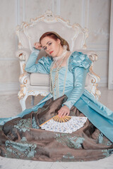 Beautiful woman in medieval style blue dress sitting on the floor near the armchair