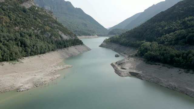 Drone forwarding shot over the verticaly long lake Ayous with receding level water during autumn season in the Pyrenees in France.