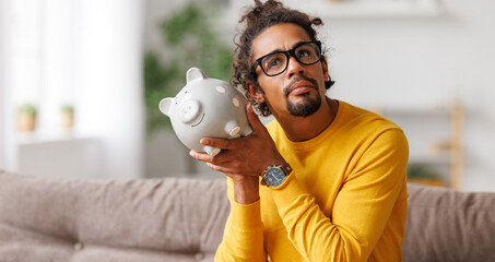 Fototapeta money problems. Poor upset african american man with piggy bank obraz