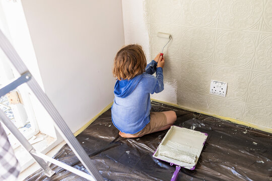 Eight year old boy using paint roller to paint a house wall