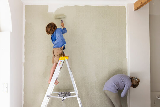 A woman and an eight year old boy decorating a room, painting walls. 