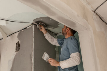 A man-a master of European appearance plasters the walls, makes repairs in the apartment, the concept of repairing and remodeling the house