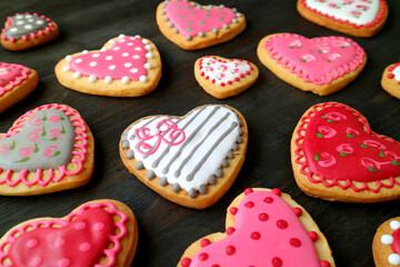Heap of beautiful heart shaped with lovely pattern cookies scattered on black wooden backdrop
