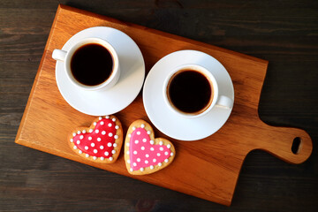 Two cups of coffee and a pair of dotted heart shaped cookies served on wooden table