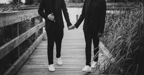 European Gay Couple holding hands, wearing black suits, wedding day of a same sex couple. Black and...