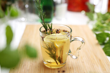 Herbal tea with rosemary, cloves, ginger, honey and lemon in a glass cup on a wooden table. Hot...