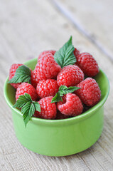 Fresh ripe raspberries in a green bowl on a wooden background. Close up.