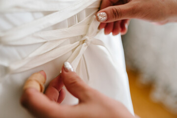 Bridesmaid helping bride fasten corset and getting her dress, preparing bride in morning for the wedding day.