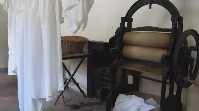 Inside of laundry room there is a vintage style drying press or mangle and white clothes drying on clothesline.