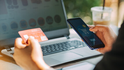 Hands holding credit card and using laptop for shopping online. New normal lifestyle of using smartphone while payment by mobile banking app from home.
