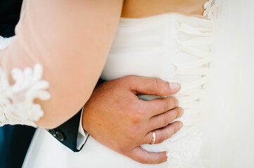 The groom embraces the bride with his hands behind the waist and standing on wedding ceremony of the outdoor in the nature backyard.