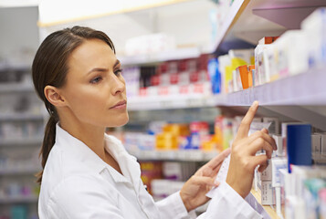 Tracking down prescriptions. Shot of an attractive young pharmacist checking stock in an aisle.