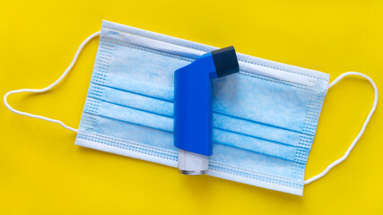 Top view of one blue inhaler and a surgical mask on a colorful yellow background. World Asthma Day.